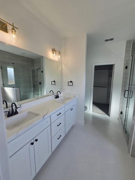 Full bathroom featuring double vanity, light tile patterned floors, a stall shower, and a walk in closet