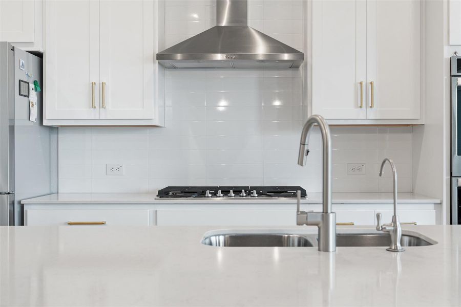 Kitchen featuring backsplash, wall chimney exhaust hood, freestanding refrigerator, and white cabinets