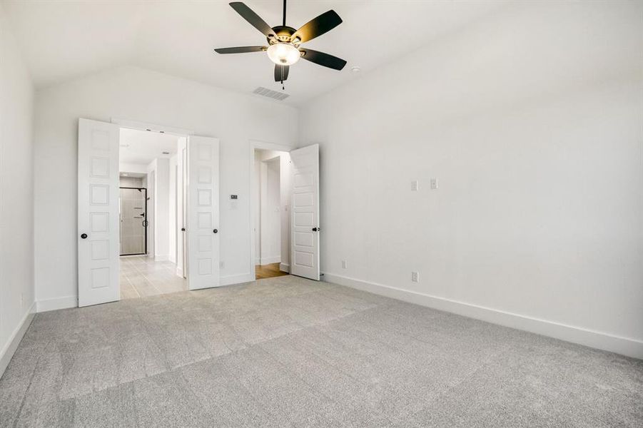Unfurnished bedroom featuring light colored carpet, a ceiling fan, vaulted ceiling, and ensuite bath