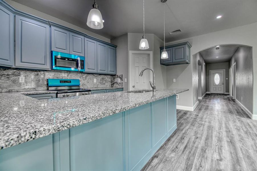 Kitchen featuring light hardwood / wood-style flooring, stainless steel appliances, decorative light fixtures, sink, and tasteful backsplash