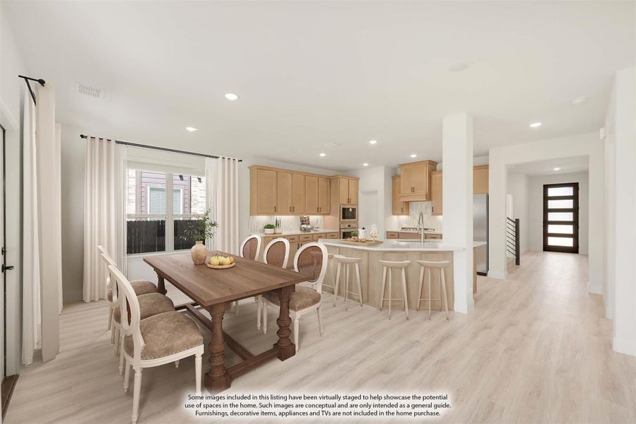 Open dining area with wood table flowing into kitchen with light wood cabinets and center island with bar seating
