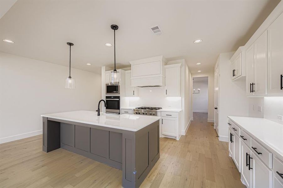 Kitchen featuring pendant lighting, recessed lighting, a center island with sink, white cabinetry, and light wood-style floors