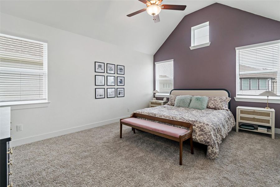 Spacious bedroom featuring vaulted ceilings, a cozy carpeted floor, and abundant natural light from multiple windows. Spacious bedroom featuring vaulted ceilings, a cozy carpeted floor, and abundant natural light from multiple windows.
