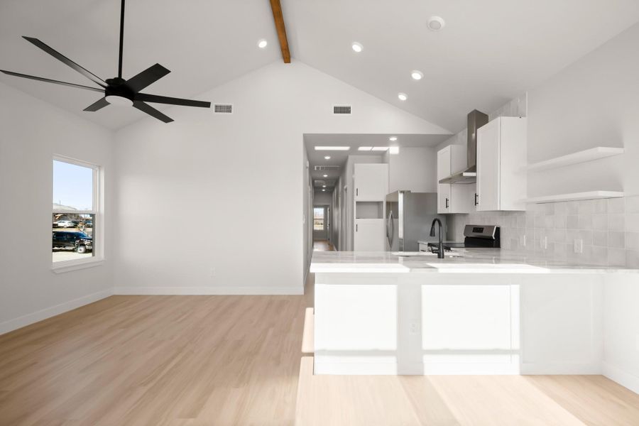 Kitchen with white cabinets, open shelves, light stone countertops, light wood finished floors, and a peninsula