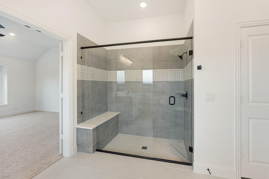 Walk-in shower with gray tile walls, glass door, built-in bench, and black hardware fixtures Walk-in shower with gray tile walls, glass door, built-in bench, and black hardware fixtures