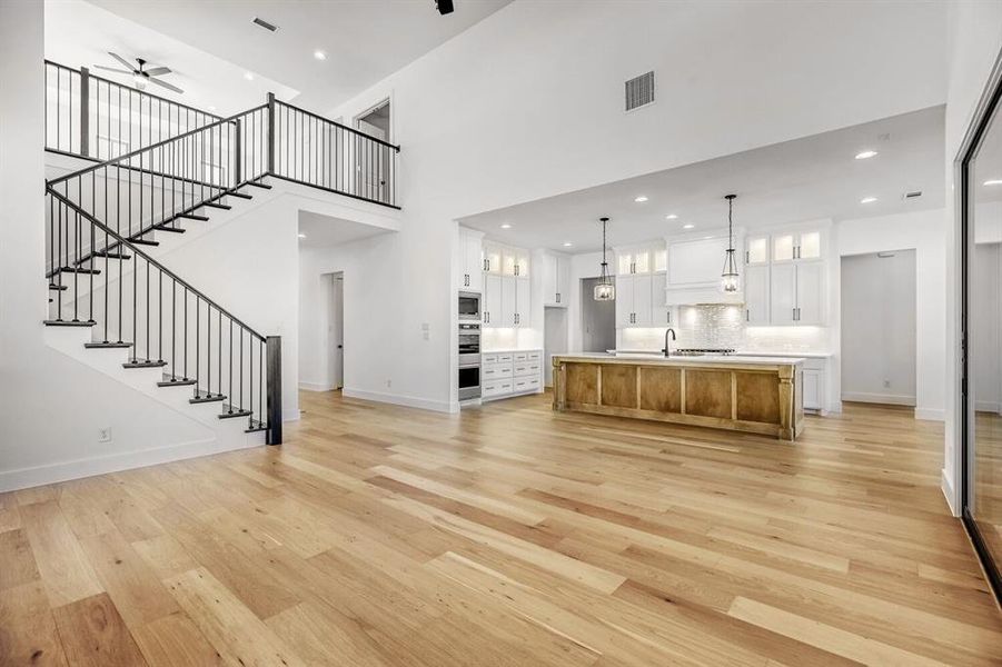 Unfurnished living room with ceiling fan, light wood-type flooring, recessed lighting, and a high ceiling