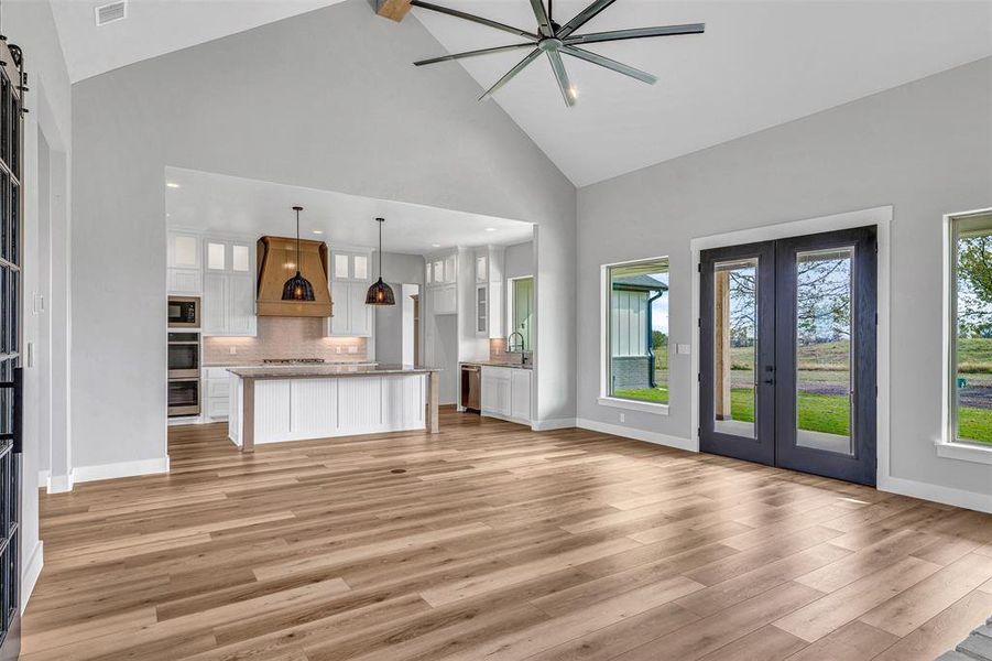 Unfurnished living room featuring sink, french doors, a barn door, high vaulted ceiling, and light wood-type flooring