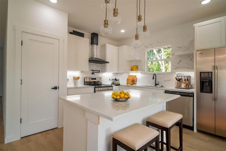 Kitchen featuring stainless steel appliances, white cabinets, wall chimney range hood, and a kitchen island