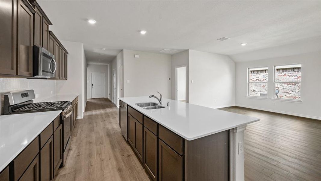 Open-concept kitchen and living area featuring wood-finish flooring, dark wood cabinetry, and recessed lighting Open-concept kitchen and living area featuring wood-finish flooring, dark wood cabinetry, and recessed lighting