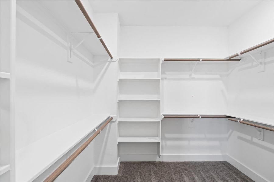 Spacious walk-in closet with white walls, shelving, and multiple hanging rods, providing ample storage and organization space. The neutral carpet flooring adds warmth and comfort. Spacious walk-in closet with white walls, shelving, and multiple hanging rods, providing ample storage and organization space. The neutral carpet flooring adds warmth and comfort.