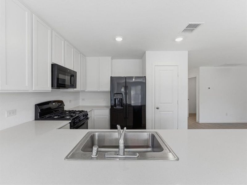 Kitchen featuring white shaker-style cabinetry, light-toned countertops, a stainless steel double-basin sink with a chrome faucet, black gas range, and a black French door refrigerator