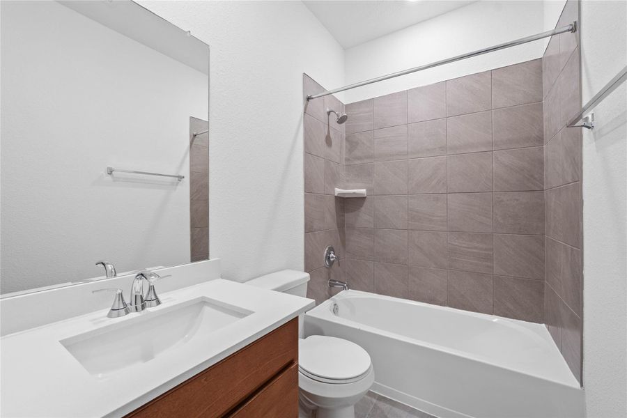 The secondary bathroom showcases tile flooring, a bath/shower combo with tile surround, a vanity with a stunning light countertop, a mirror, sleek fixtures, and contemporary finishes throughout.