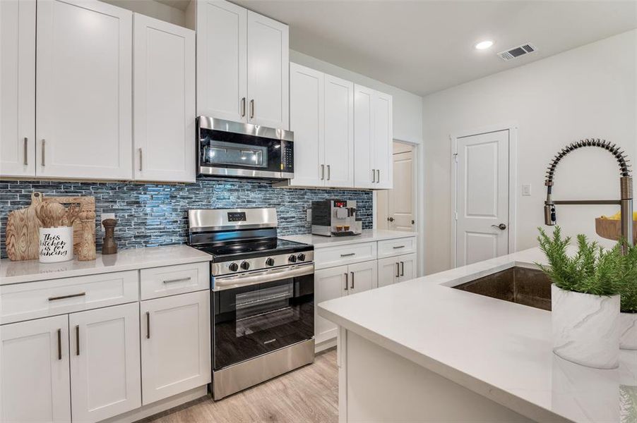 Kitchen featuring appliances with stainless steel finishes, decorative backsplash, white cabinetry, and recessed lighting