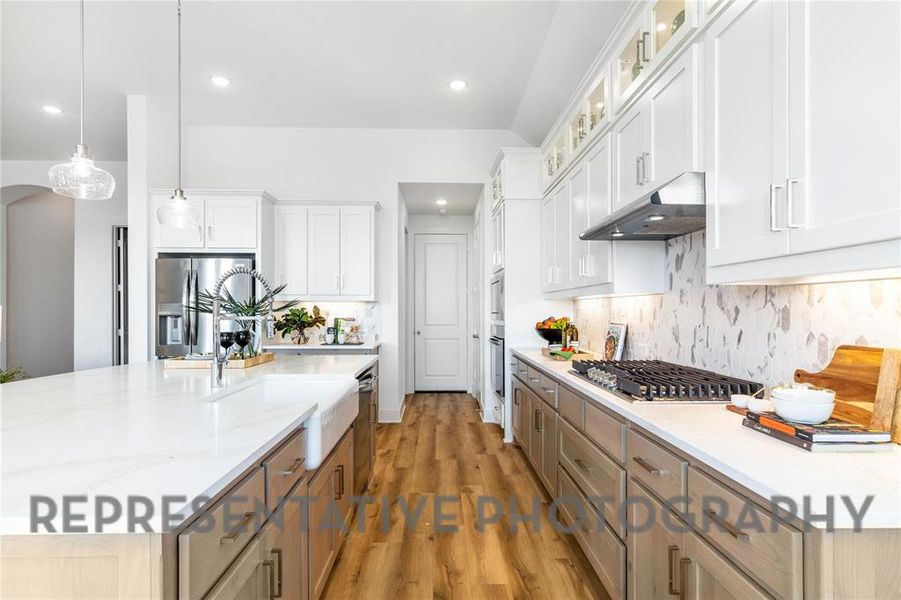 Kitchen featuring appliances with stainless steel finishes, pendant lighting, light wood-style floors, and tasteful backsplash Kitchen featuring appliances with stainless steel finishes, pendant lighting, light wood-style floors, and tasteful backsplash