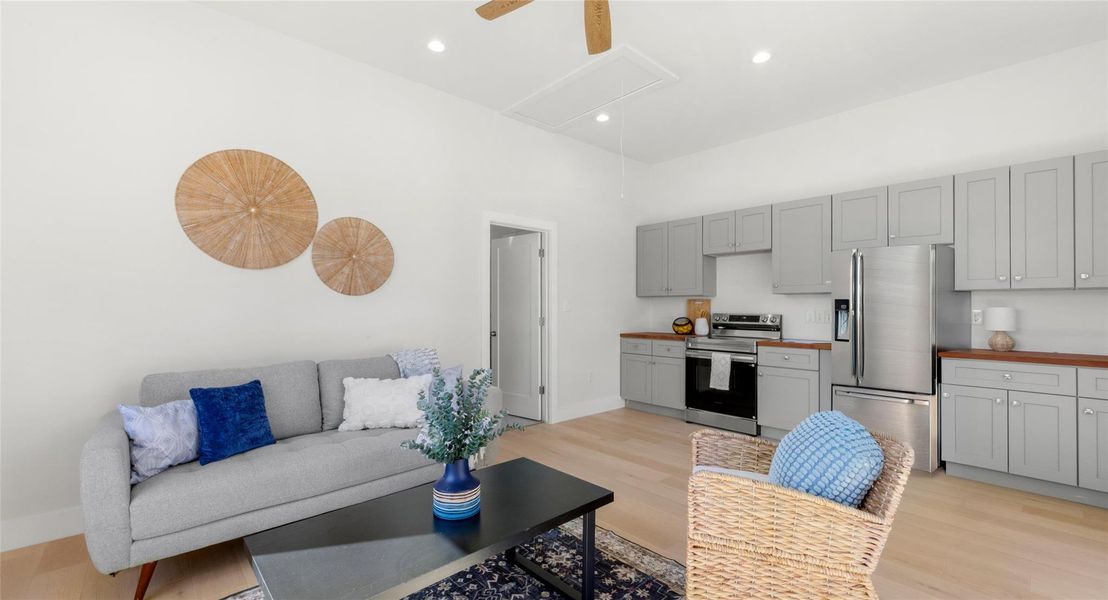 Living room featuring light wood finished floors, ceiling fan, a high ceiling, and recessed lighting