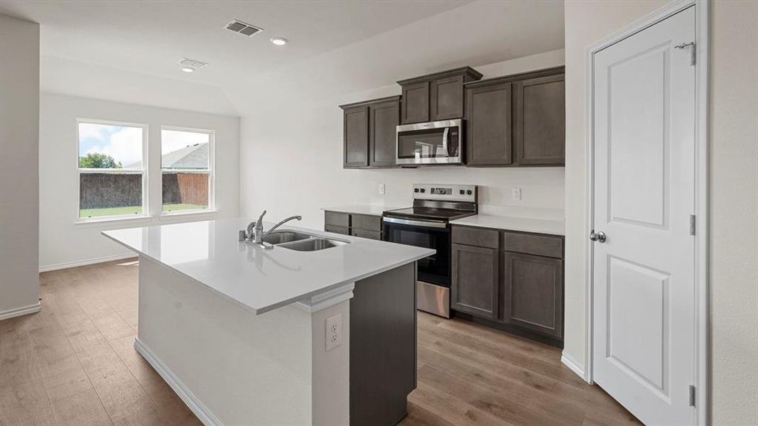 Kitchen featuring a central island with a double basin sink, stainless steel appliances, dark wood-finish cabinetry, white countertops, and wood-finish flooring