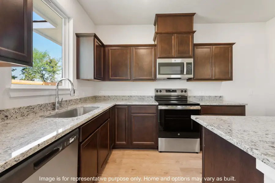 Kitchen with stainless steel appliances, dark wood finish cabinetry, light stone counters, and light wood-style floors