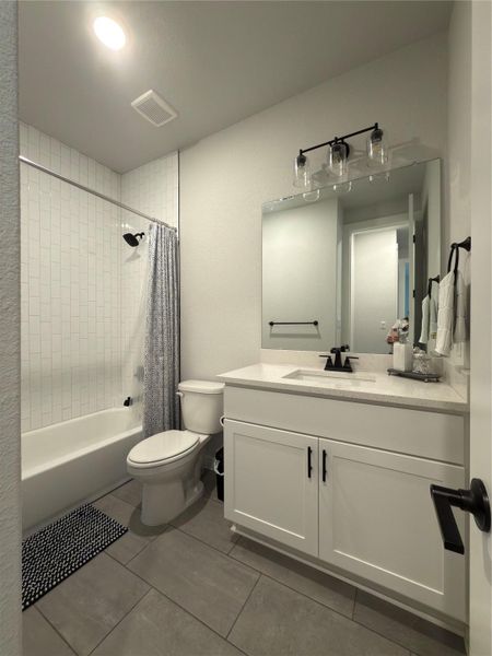 Bathroom featuring a white vanity with a light-toned countertop, black fixtures, rectangular mirror, and gray tile flooring
