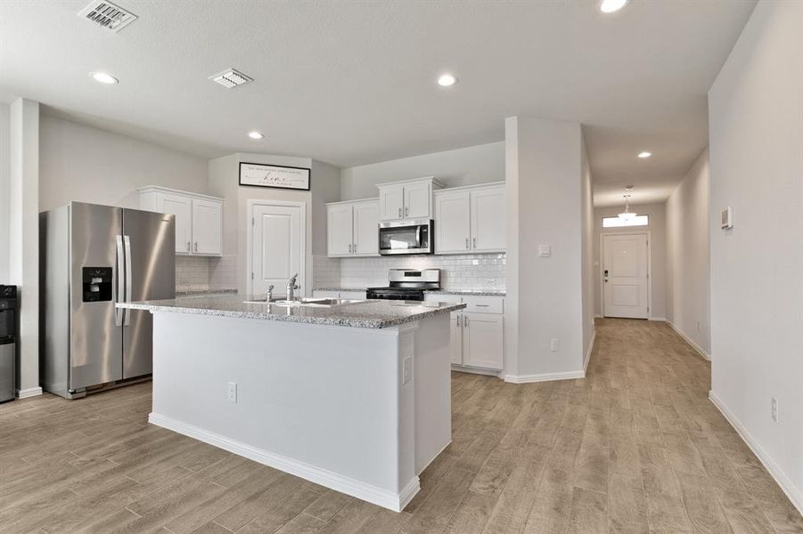 Kitchen with appliances with stainless steel finishes, white cabinetry, tasteful backsplash, light stone countertops, and a center island with sink