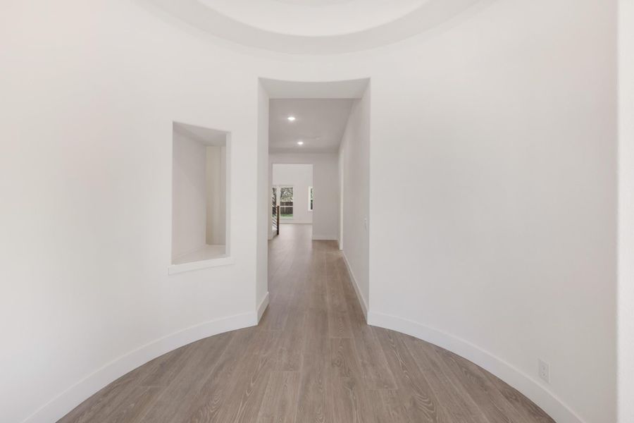 Curved entryway with round ceiling detail, wall niche, and wood-look floors leading to a hallway