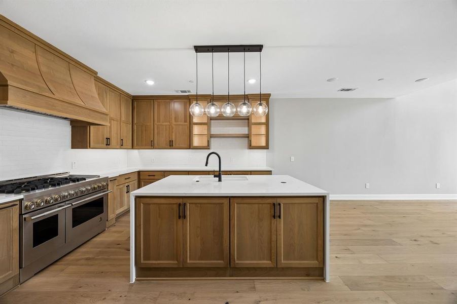 Kitchen with light wood-type flooring, range with two ovens, a kitchen island with sink, light stone countertops, and wood finish cabinets Kitchen with light wood-type flooring, range with two ovens, a kitchen island with sink, light stone countertops, and wood finish cabinets
