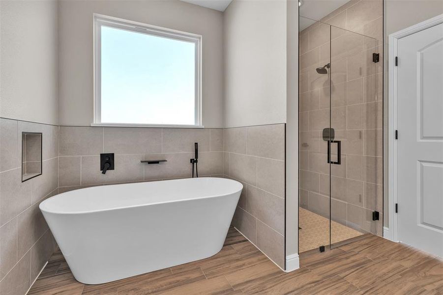 Bathroom featuring a freestanding tub, a shower stall, wood finished floors, tile walls, and a wainscoted wall Bathroom featuring a freestanding tub, a shower stall, wood finished floors, tile walls, and a wainscoted wall