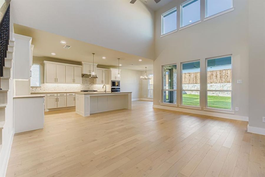 Kitchen featuring white cabinets, a center island with sink, open floor plan, decorative backsplash, and decorative light fixtures
