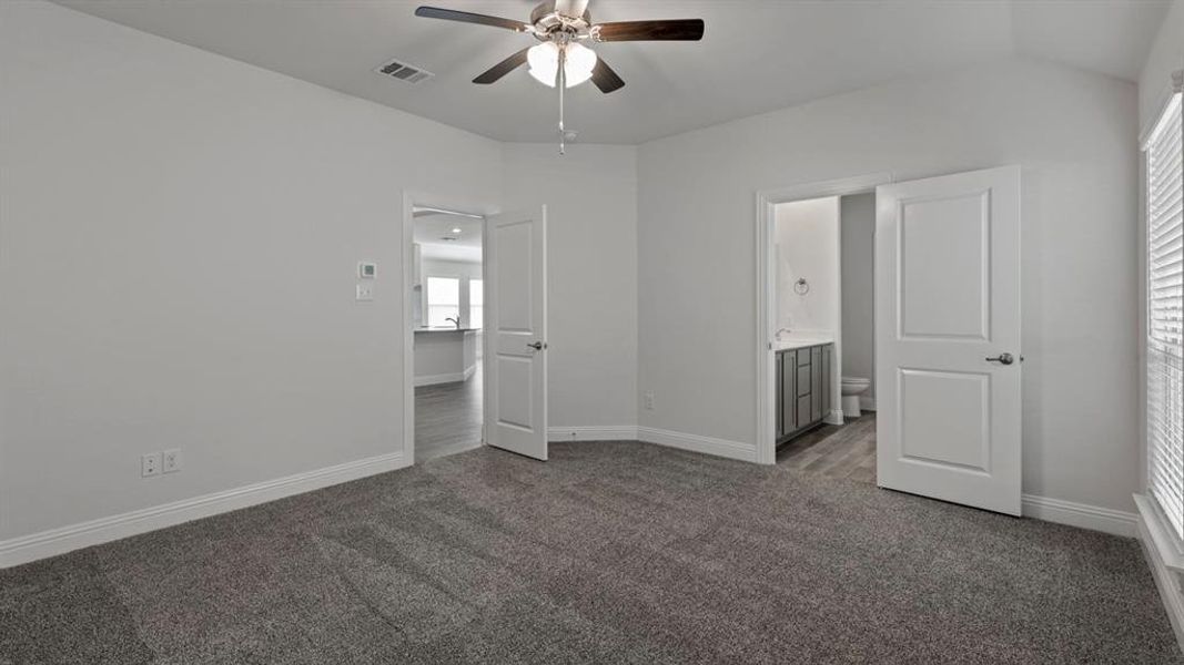 Unfurnished bedroom with ensuite bathroom, dark carpet, ceiling fan, and vaulted ceiling