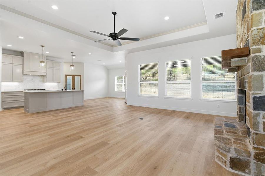 Unfurnished living room featuring light wood-style flooring, a tray ceiling, a ceiling fan, recessed lighting, and a stone fireplace Unfurnished living room featuring light wood-style flooring, a tray ceiling, a ceiling fan, recessed lighting, and a stone fireplace