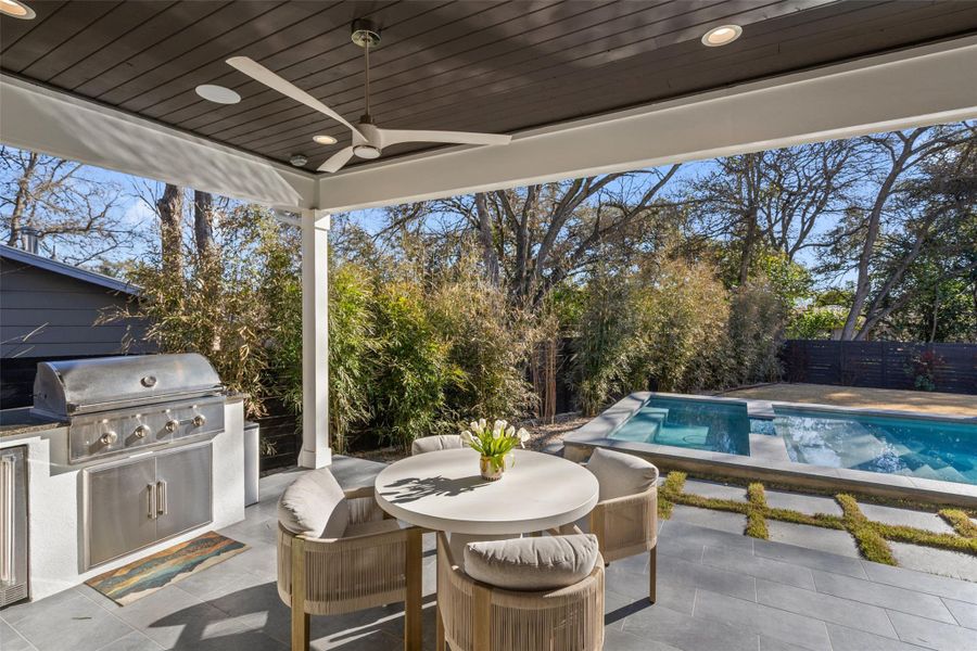 Outdoor entertainers dream! Covered back patio with surround sound speakers, built-in grill and mini refrigerator, overlooking the spacious backyard and heated pool.  Tile flooring, stained tongue and groove porch ceiling, dual fans and ambient lighting make this area feel like an extension of your living room - perfect for hosting.