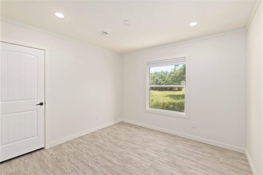 Room featuring recessed lighting, light wood-finish flooring, a white paneled door with black hardware, white baseboards, and a window with a white frame and blinds