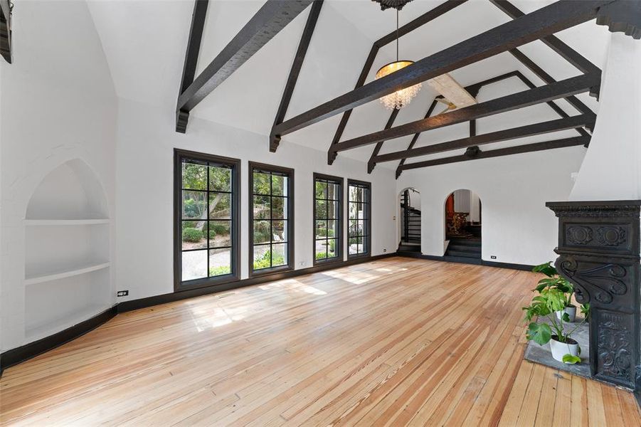 Unfurnished living room with arched walkways, a high ceiling, light wood-style flooring, and built in shelves