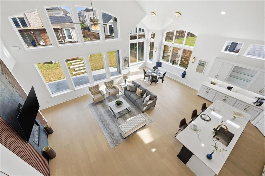 Soaring ceilings featuring a full wall of varied fenestration, wood-finish flooring, a modern kitchen island with an integrated sink and breakfast bar, a built-in fireplace, and recessed lighting