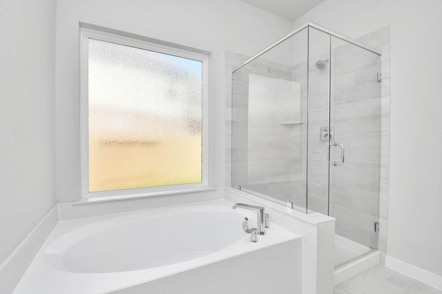 Indulge in a spa-like retreat within the confines of this primary bathroom. Delight in a spacious walk-in shower enveloped in stylish tile surround and unwind in a separate garden tub adorned with custom detailing. Sample photo of completed home with similar floor plan. Actual colors and selections may vary.