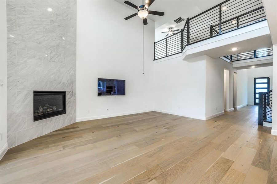 Unfurnished living room featuring a fireplace, a high ceiling, ceiling fan, and wood finished floors