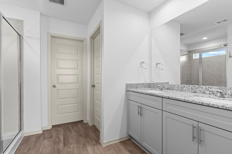 Primary bathroom entrance with easy-care wood-look vinyl plank floors, his and her private undermount sinks with granite countertops, and tall shaker cabinetry offering both function and style. Make that call so we can open the door to the monster size walk in closet! Primary bathroom entrance with easy-care wood-look vinyl plank floors, his and her private undermount sinks with granite countertops, and tall shaker cabinetry offering both function and style. Make that call so we can open the door to the monster size walk in closet!