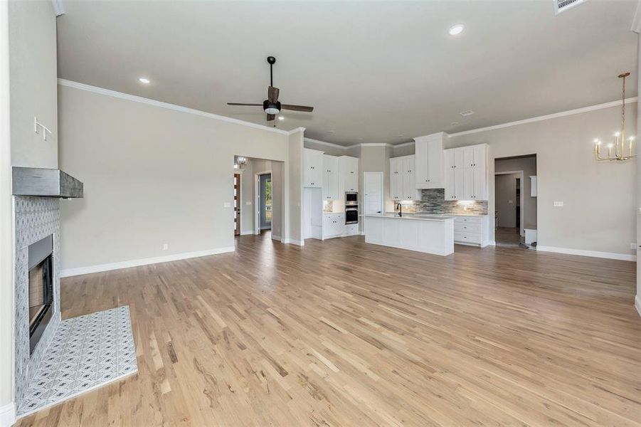 Unfurnished living room with ceiling fan with notable chandelier, light hardwood / wood-style flooring, sink, and ornamental molding