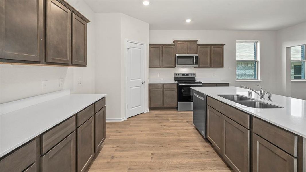 Spacious kitchen featuring an expansive island with dual sinks, white countertops, coordinating backsplash, stainless steel appliances, and wood-finish flooring