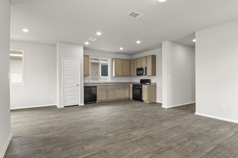 Image of two story home living room with brown flooring and light grey walls with a kitchen in the distance Image of two story home living room with brown flooring and light grey walls with a kitchen in the distance