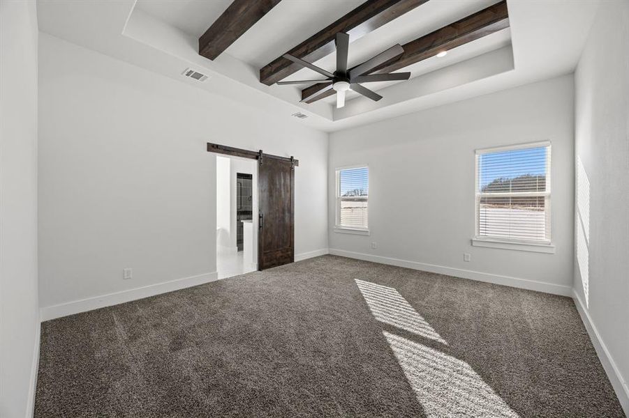 Unfurnished bedroom with a barn door, beamed ceiling, carpet, ceiling fan, and a tray ceiling