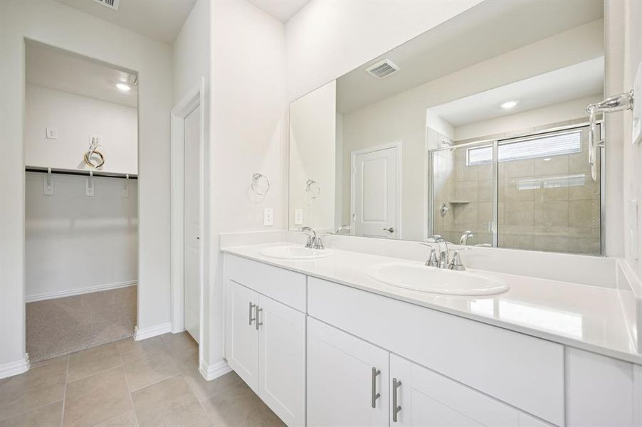 Full bathroom with double vanity, a spacious closet, a shower stall, and light tile patterned floors