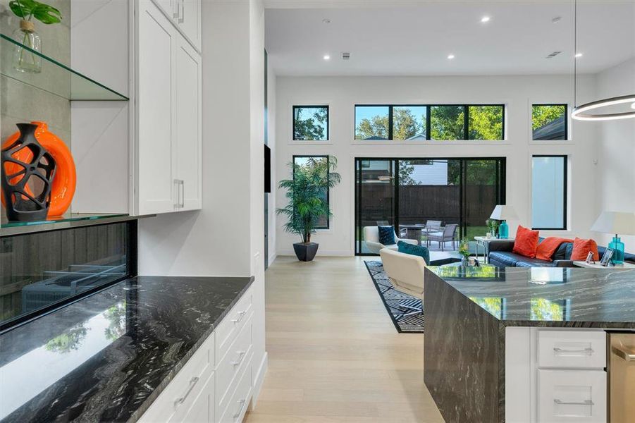 Kitchen with dark stone countertops, white cabinetry, hanging light fixtures, light wood-style floors, and open floor plan Kitchen with dark stone countertops, white cabinetry, hanging light fixtures, light wood-style floors, and open floor plan