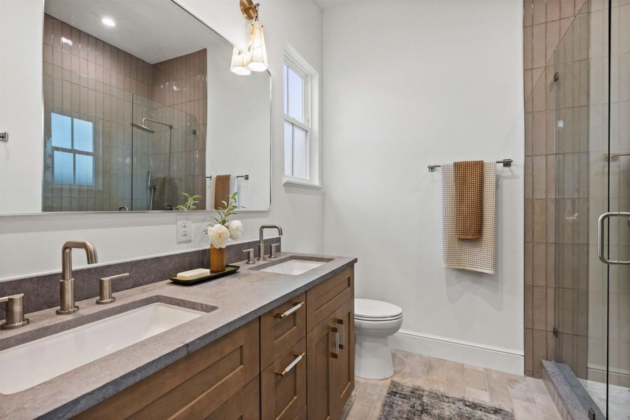 Dual vanities with stone counters and a spacious glass-enclosed shower create a tranquil bathroom retreat.