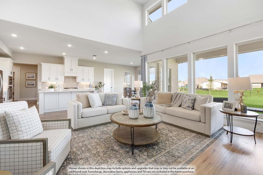 Open-concept living room with high ceilings, large windows, hardwood floors, and kitchen visible in background