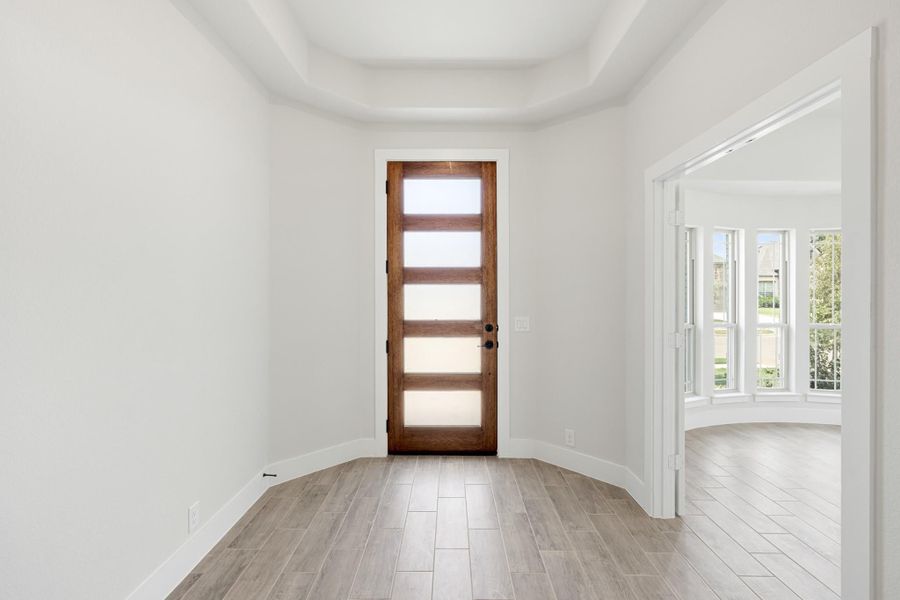 Bright entryway with wood and glass front door, tray ceiling, and light tile floors