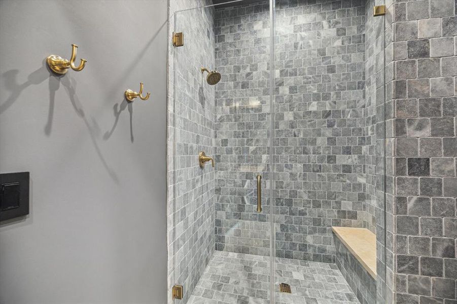 Luxurious stone-tiled shower featuring a glass door and high-end brass fixtures. The natural stone finish gives it a spa-like ambiance with a built-in bench for extra comfort.