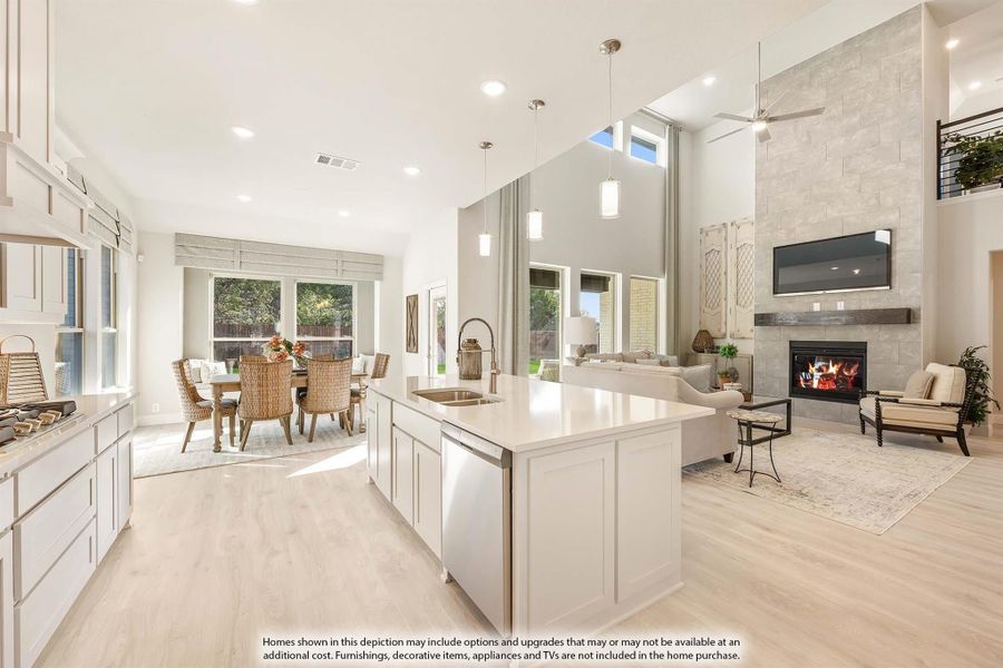 Open-concept kitchen with white island, flowing into dining area and living room with stone fireplace and high ceilings