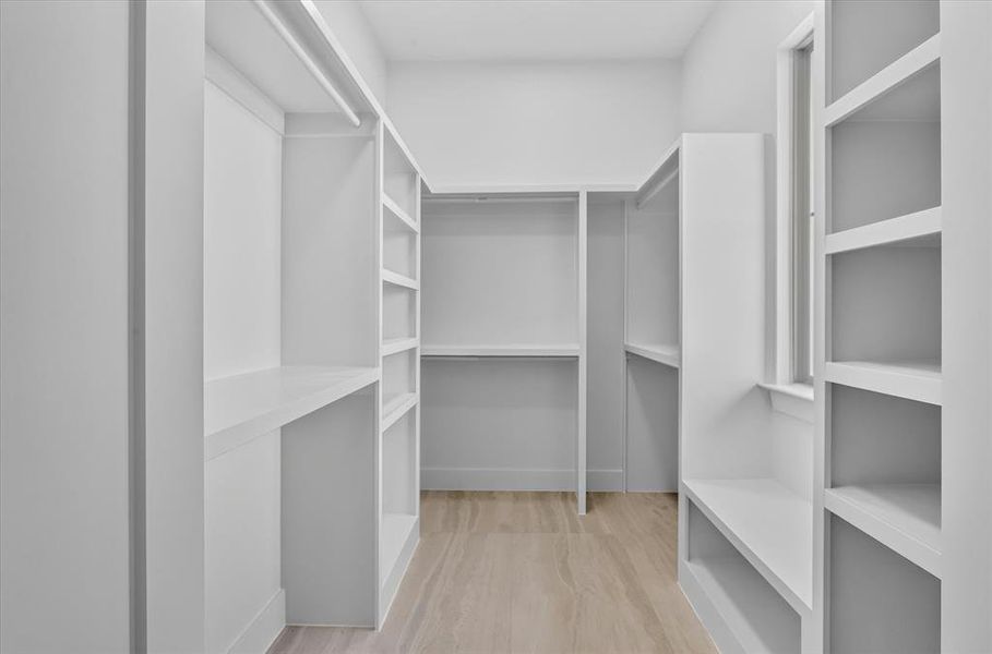 Walk-in closet featuring extensive built-in shelving, hanging rods, an integrated window, and wood-finish flooring