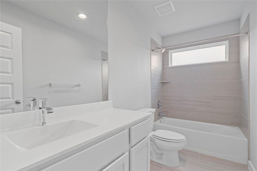 Secondary bath features tile flooring, bath/shower combo with tile surround, white stained wood cabinets, beautiful light countertops, mirror, dark, sleek fixtures and modern finishes.