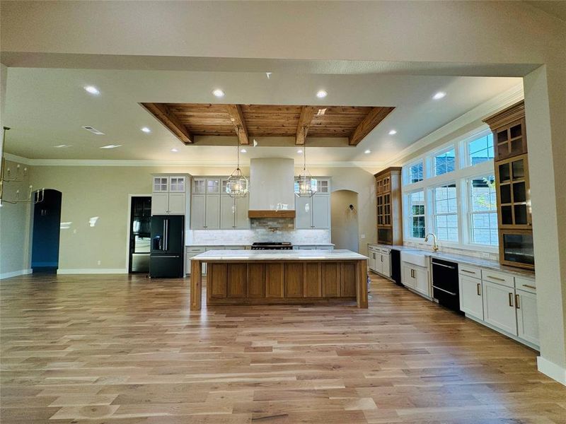 Kitchen featuring hanging light fixtures, a large island, black appliances, light wood-type flooring, and white cabinets